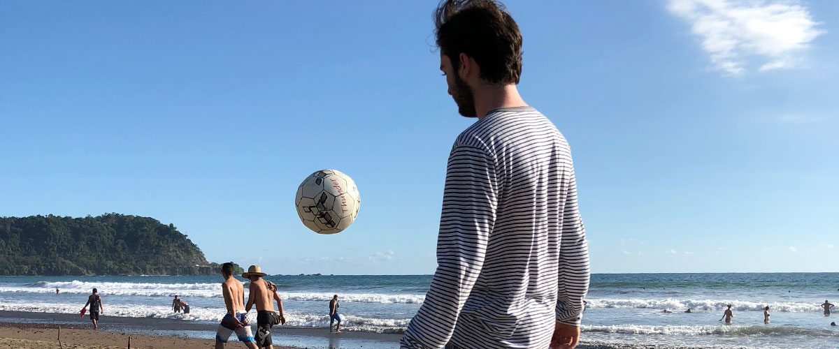 Student kicking a soccer ball on a beach